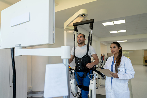Latin American patient doing physiotherapy with an exoskeleton guided by a physical therapist - healthcare and medicine concepts