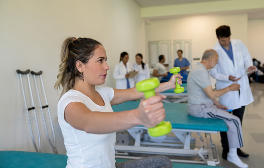 Young woman lifting weights while exercising in physiotherapy - healthcare and medicine concepts