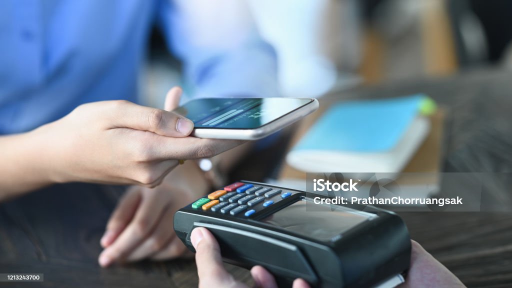 Cropped image of smart man's hands holding a smartphone and doing a payment by using a NFC technology at the Credit card reader that putting on cafe payment counter. Technology and Payment concept. Mobile Payment Stock Photo