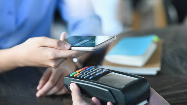 Cropped image of smart man's hands holding a smartphone and doing a payment by using a NFC technology at the Credit card reader that putting on cafe payment counter. Technology and Payment concept. Cropped image of smart man's hands holding a smartphone and doing a payment by using a NFC technology at the Credit card reader that putting on cafe payment counter. Technology and Payment concept. mobile payment photos stock pictures, royalty-free photos & images