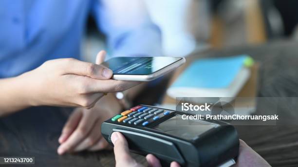 Cropped Image Of Smart Mans Hands Holding A Smartphone And Doing A Payment By Using A Nfc Technology At The Credit Card Reader That Putting On Cafe Payment Counter Technology And Payment Concept Stock Photo - Download Image Now