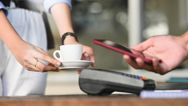 istock Cropped image of smart man's hands holding a smartphone and doing a payment by using a NFC technology at the Credit card reader that putting on cafe payment counter. Technology and Payment concept. 1213243826