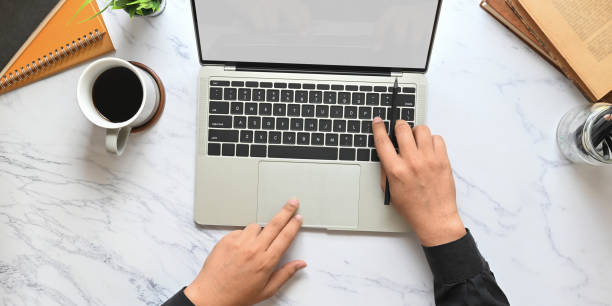 istock Top view image of businessman's hands using a computer tablet with white blank screen that putting on marble texture table with coffee cup, notebook, books, potted plant and pencil holder. 1213244228