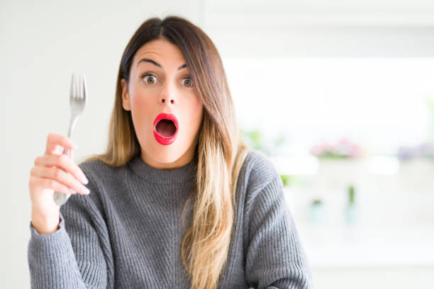 istock Young beautiful woman holding silver fork at home scared in shock with a surprise face, afraid and excited with fear expression 1213246248