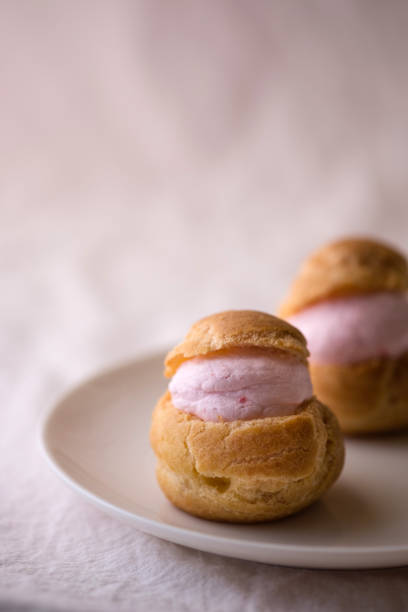 Homemade choux cream or cream puffs with strawberry cream on pink background.