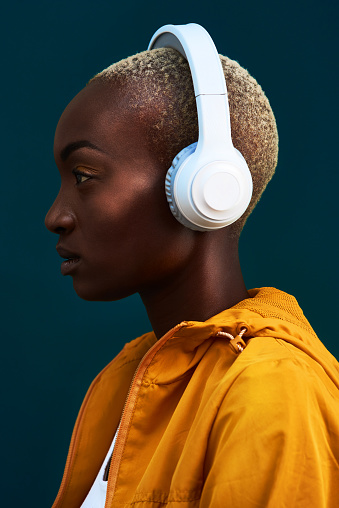 Cropped shot of an attractive young sportswoman standing alone against a dark background and listening to music through headphones