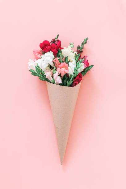 Roses bouquet in cone on pink background, flat lay, top view.