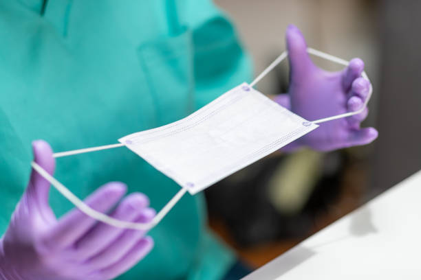 Hands in protective gloves holding protective mask Hands in protective gloves holding stretching bands on protective mask for application putting on latex gloves stock pictures, royalty-free photos & images