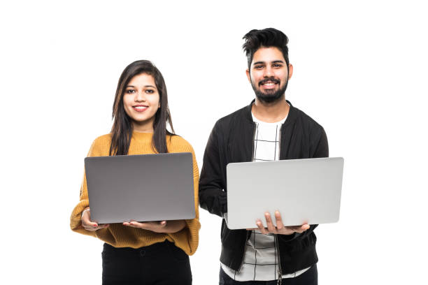 istock Portrait of a young indian couple holding laptops computer while standing isolated over gray wall background 1213259178