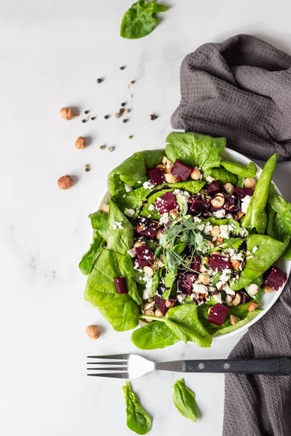 istock Beet salad with fresh spinach, chickpea, soft cheese and hazelnut with fork on light grey background with copy space. Top view. 1213260872
