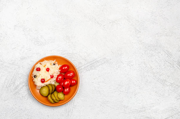 Homemade fermented products on a plate, sauerkraut, pickled tomatoes, pickles, light gray background.
