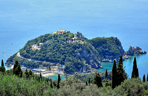 Paleokastritsa / Corfu, Greece - A semicircular mountain covered with green trees on a cape surrounded by the Ionian Sea, at the top of the Monastery of the Life-Giving Spring, in the summer.