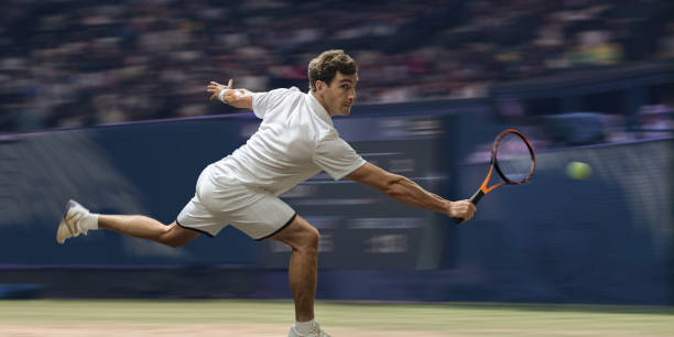 Professional Male Tennis Player In Mid Motion On Grass Court A close up view of a professional male tennis player running in mid motion reaching out above to strike the tennis ball in a volley from close to the baseline. The athlete is playing on a grass court in a generic stadium full of spectators. With motion blur. tennis outfit stock pictures, royalty-free photos & images