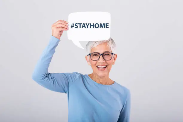 Photo of Mature woman holding Stay home phrase #stayhome on speech bubble isolated on background.