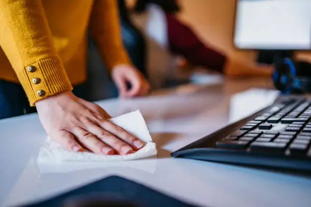 Photo of Woman cleaning computer desk in office