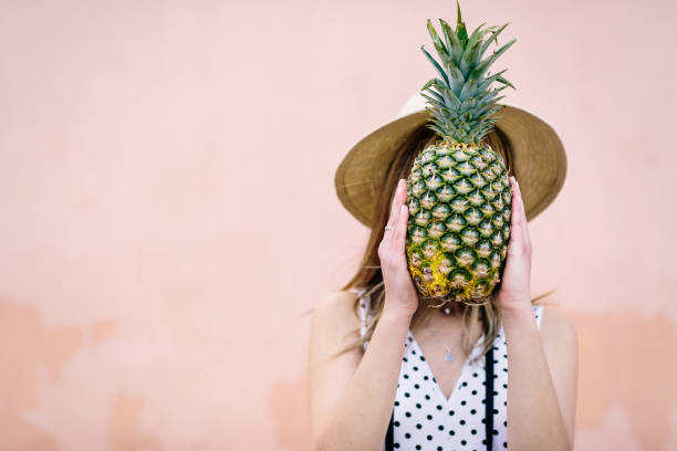 istock Young girl in hat covers her face with a pineapple 1213279651