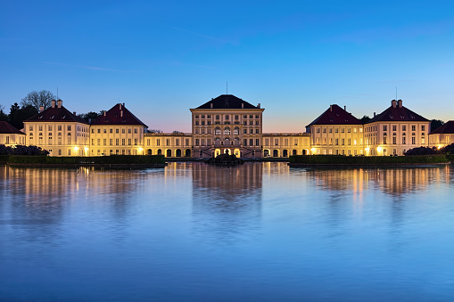 Munich, Germany - May 16, 2017: Nymphenburg Palace at sunset. Eastern facade reflects in the water parterre formed by the endpoint of the eastern canal of Nymphenburg. The palace was built in 1664-1675 by design of the Italian architect Agostino Barelli.