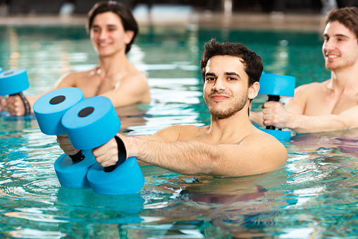 Selective focus of man with barbells smiling at camera while exercising in swimming pool
