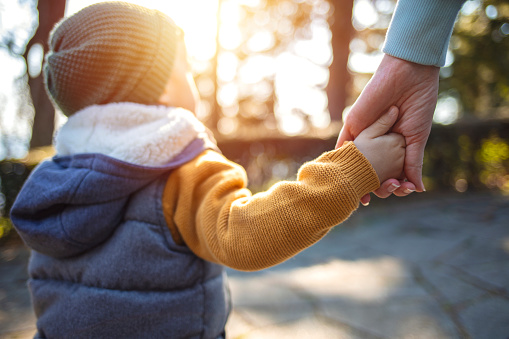 Close up of mother and a child hands at the sunset. A parent holds the hand of a small boy in the sunset. Mother holding her little boys hand walking down the street