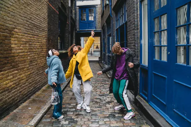 Three happy friends dancing together in the city. Mixed race and african ethnicities. They are wearing cool clothes and dancing in Shoreditch, London.