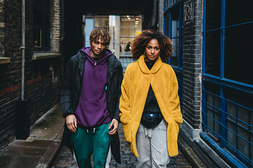 Young couple walking in the street. They are wearing colorful clothes and looking at camera. Shoreditch, London.