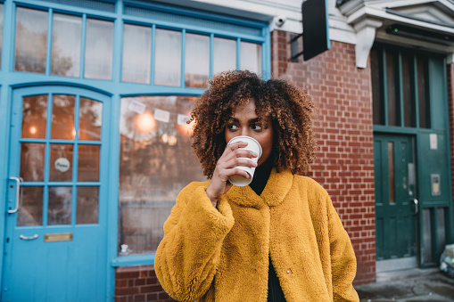 Portrait of a young adult beautiful woman drinking coffee. She's looking away. Mixed race and afro hair.