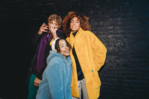 Three friends dancing in the city against a black brick wall
