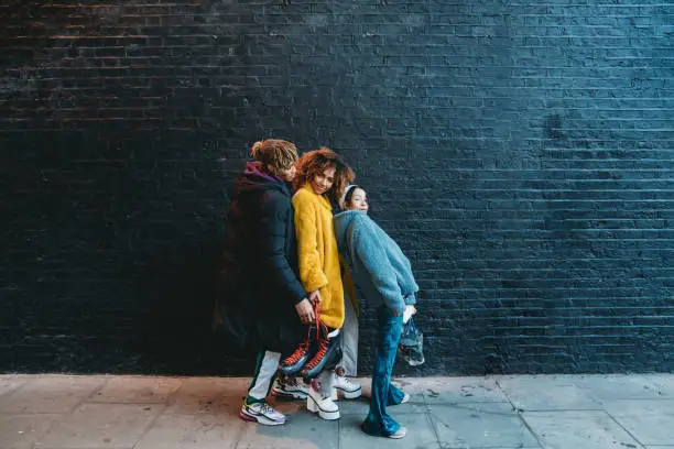 Photo of Three friends dancing in the city against a black brick wall