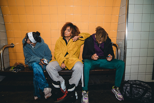 Three friends waiting for the train in a subway station. The young adult man is playing with a mobile app.