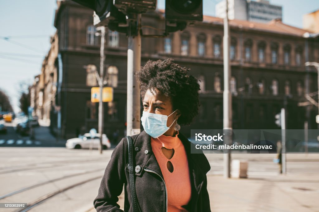 Portrait Of Young Woman With Mask On The Street. Young Afro American woman standing on city street with protective mask on her face. Virus pandemic and pollution concept. Air Pollution Stock Photo