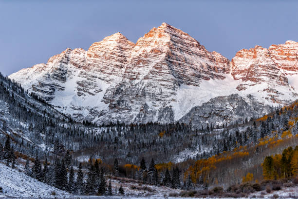 alba mattutina maroon bells con sole in vetta ad aspen, colorado montagna rocciosa e vista sul fogliame giallo autunnale e neve invernale - maroon foto e immagini stock