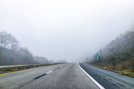 Fog mist road highway driving in rural countryside in West Virginia with mile marker near New River Gorge in morning