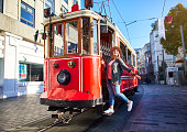Beautiful young girl tourist in a hat poses in front of tram at popular Istiklal street in Beyoglu, Istanbul, Turkey