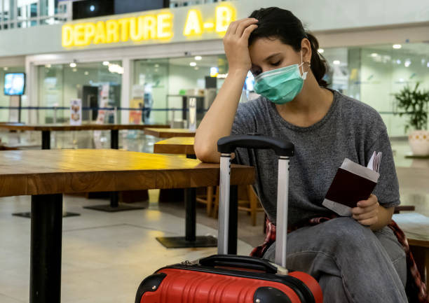 zrozpaczona, zestresowana podróżniczka z maską medyczną na twarzy czeka na nieudany, opóźniony lub odwołany lot z powodu koronawirusa. - nieudany zdjęcia i obrazy z banku zdjęć