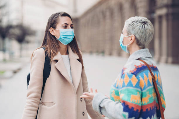 istock Two women with protective masks talking on the street 1213309860