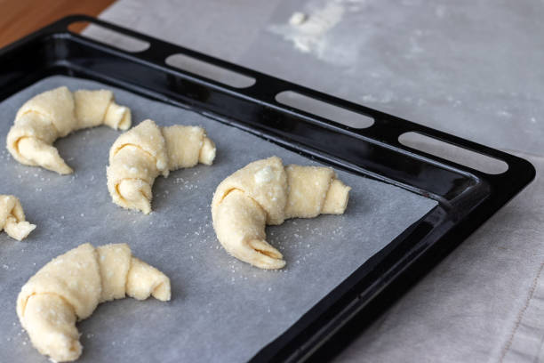 istock Croissants from a raw cottage cheese dough prepared for baking sprinkled with sugar on a baking sheet covered with parchment baking paper before loading into the oven. Process of making curd bagels 1213318418