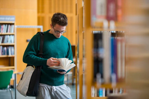 istock Student Flipping Through Pages of a Book in Library 1213321529