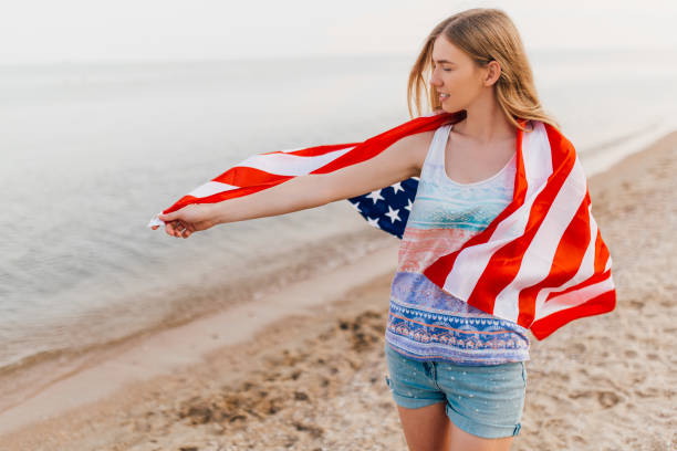 istock happy woman outdoors on a beach holding a US flag and having fun 1213330604