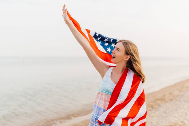 istock happy woman outdoors on a beach holding a US flag and having fun 1213331459