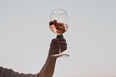 Glass of wine with splashes in woman's hand against the sunset sky.