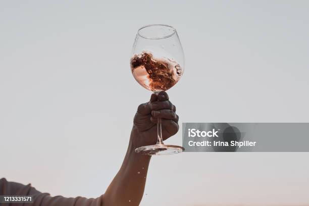 Glass Of Wine With Splashes In Womans Hand Against The Sunset Sky Stock Photo - Download Image Now