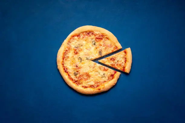 Pizza quattro formaggi made at home. Sliced pizza on a blue background, above view. Italian pizza made with 4 types of cheese.