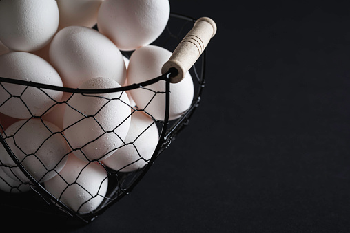 White eggs in an iron basket on black table, in low light. Fresh chicken eggs, a rich source of proteins.