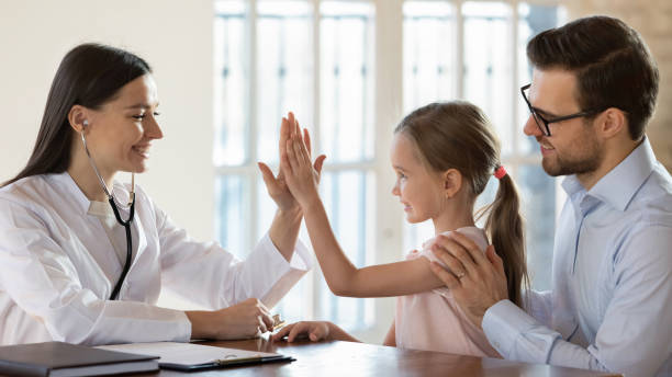 Smiling female doctor nurse giving high five to little patient Side view smiling female doctor nurse giving high five to little preschool girl sitting on daddy's lap. Pleasant general practitioner getting acquainted with small patient at checkup in modern clinic. general view stock pictures, royalty-free photos & images