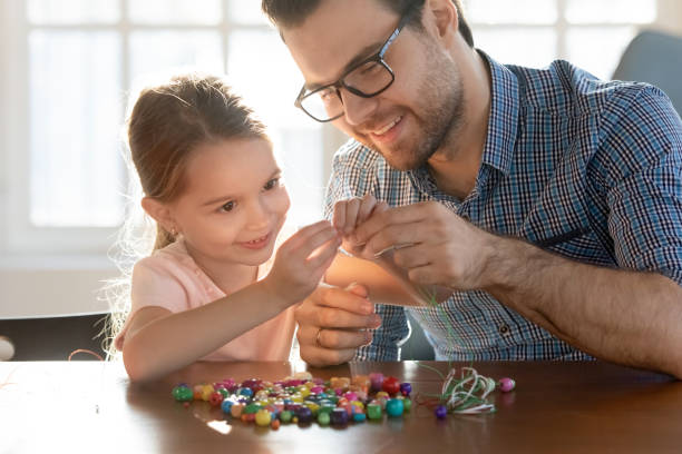 istock Smiling young daddy helping small preschool daughter making bracelets. 1213336937