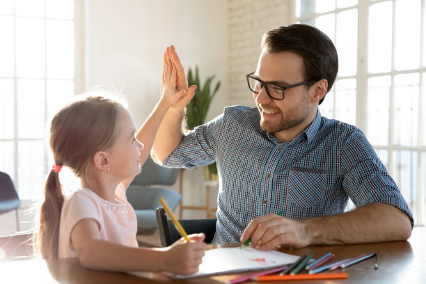 Little child girl giving high five to affectionate loving father. Head shot happy little child girl giving high five to affectionate loving father, finishing drawing picture together at home. Smiling young dad celebrating good work done with cute small daughter. homework stock pictures, royalty-free photos & images