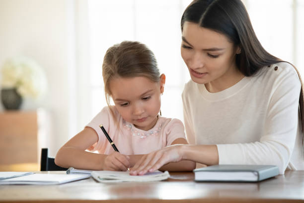 ласковая молодая мать учит маленькую дочь чтению письма. - reading and writing classroom alphabet learning стоковые фото и изображения