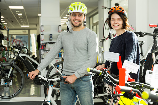 Portrait of man and woman in helmet standing with bike in the store