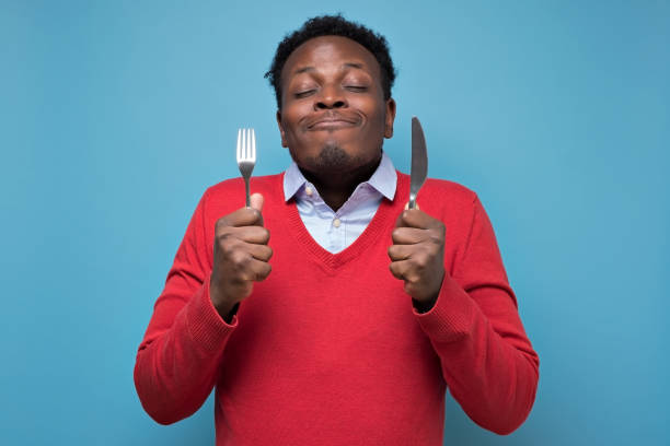 istock crazy african american man in red sweater holding a fork and a knife. 1213339699