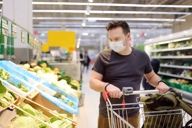 hombre que lleva máscara médica desechable comprando en el supermercado durante el brote de neumonía por coronavirus - fotografía temas fotografías e imágenes de stock